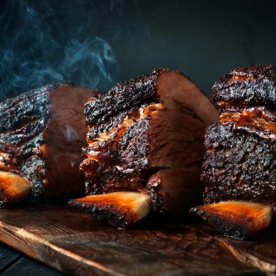 Smoked beef ribs with a dark, crispy crust on a wooden board.