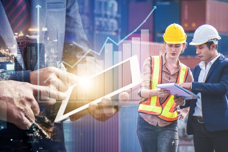 Businessman use tablet show growth revenue graph info and engineer partner stand at container yard, loading containers box from cargo freight ship for import and export, teamwork partnership concept.