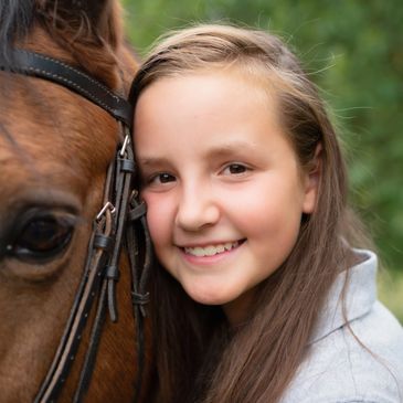 A girl smiling closely beside a brown horse.