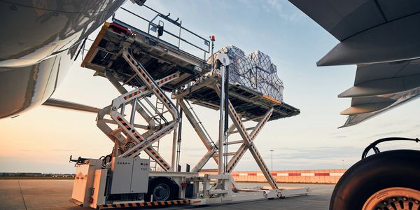 Cargo being loaded onto an airplane using a hydraulic lift at an airport.