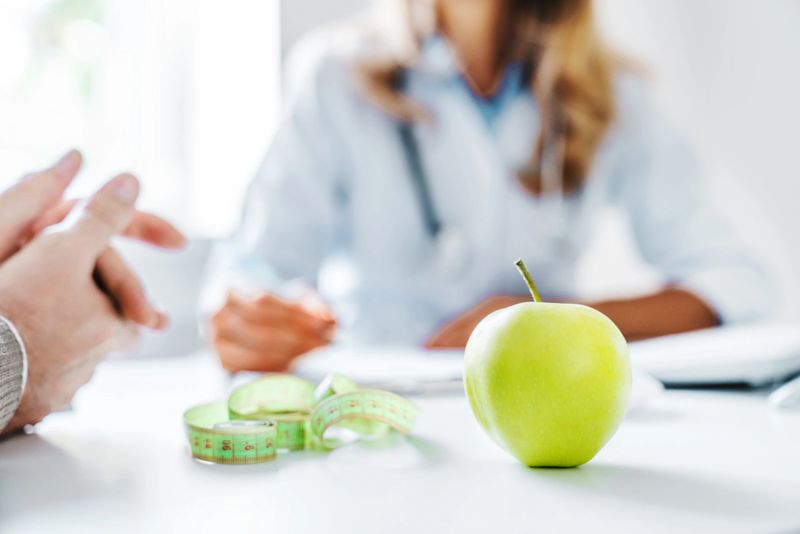 Healthy food concept. Cropped close up of woman doctor dietician recommending senior male patient fresh apple