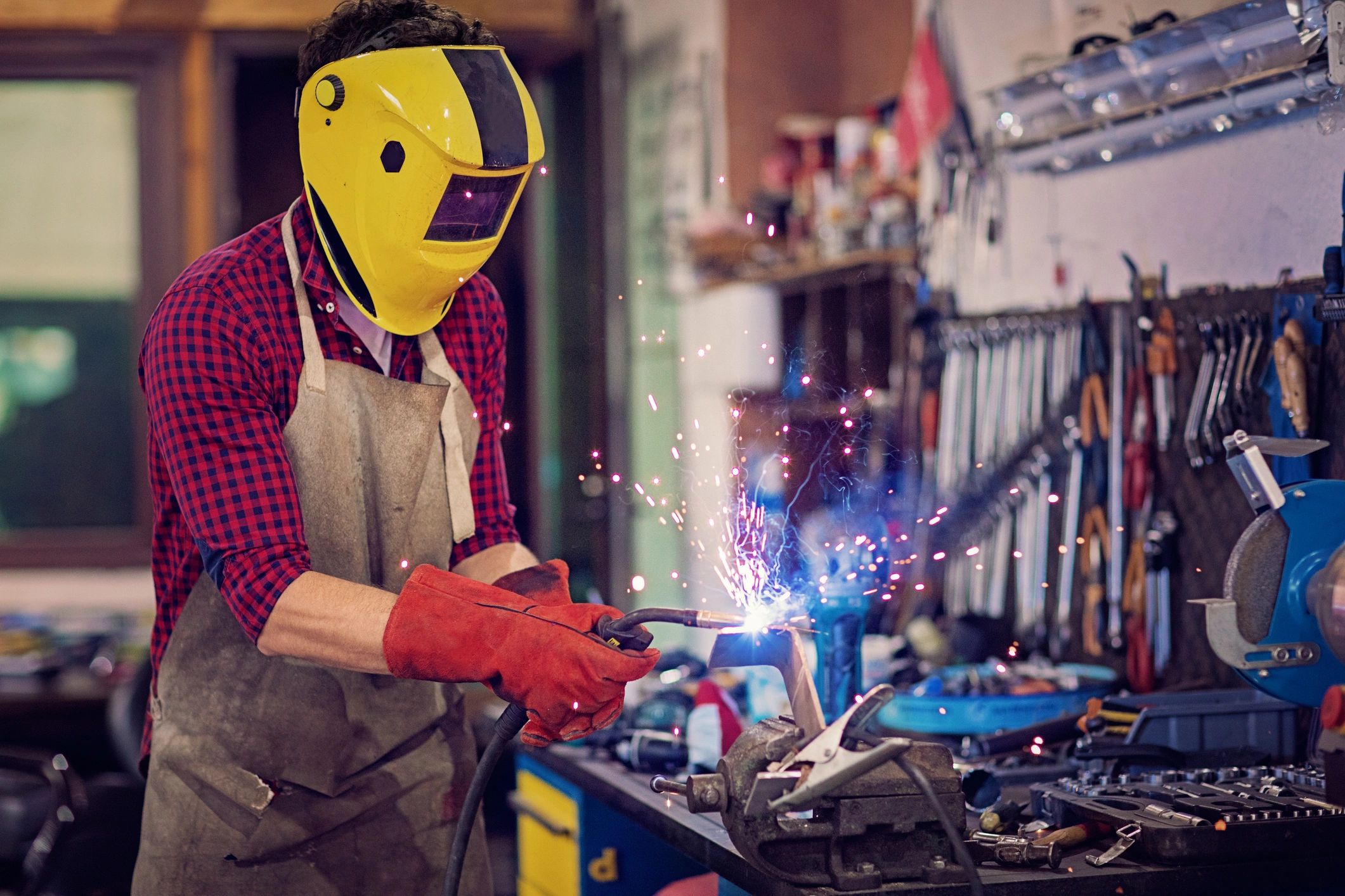 Person welding metal in a workshop with protective gear and sparks flying.