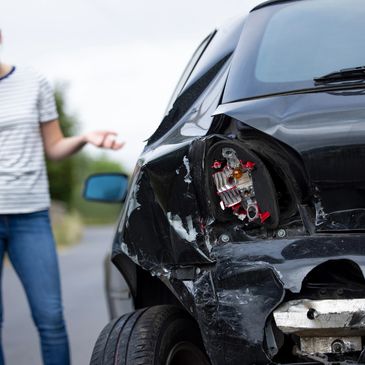 Woman on phone beside a badly damaged black car after an accident.