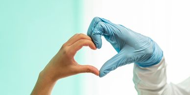 A person and a gloved hand form a heart shape together.