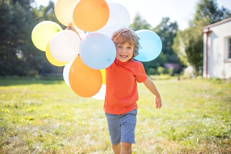 A joyful child laughing while playing with colorful balloons, captured in soft natural light.
