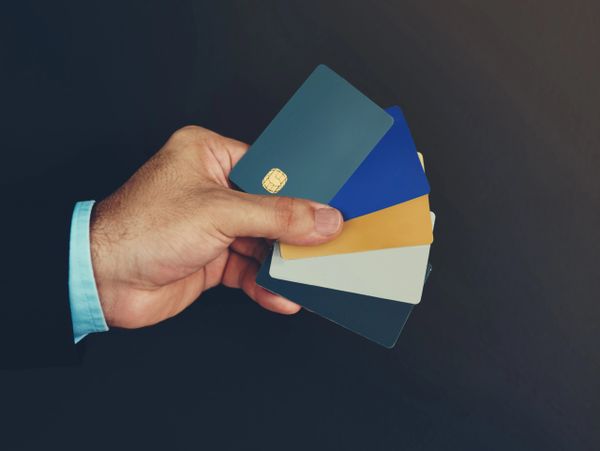 Hand holding multiple colored credit cards against a dark background.