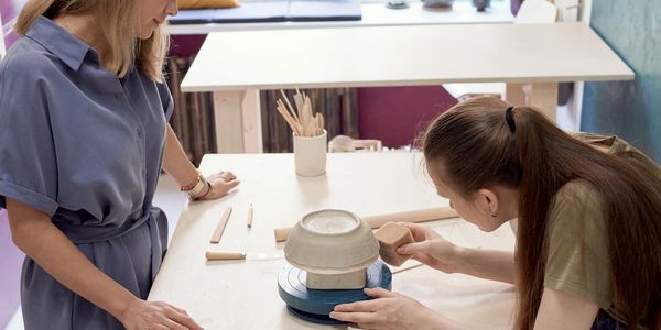 Two women working on a pottery project in a bright studio.