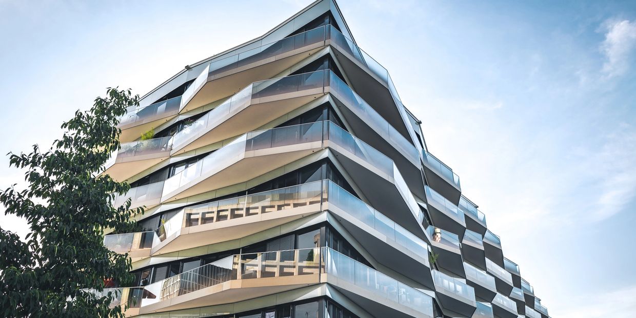 Modern apartment building with angled balconies and glass railings under a clear sky.