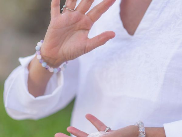 Person wearing white with hands showing spiritual jewelry and holding a crystal.