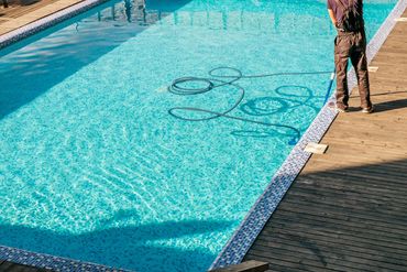 Person cleaning a swimming pool with a vacuum.