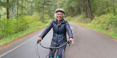 Happy elderly woman cycling on a forest road wearing a helmet and jacket.