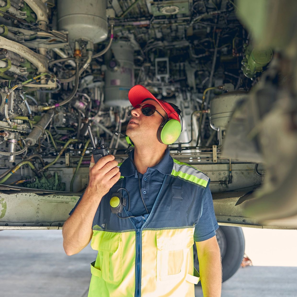Aircraft maintenance worker inspecting engine components with radio communication.