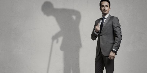 A man in a suit casting an old man shadow with a cane.