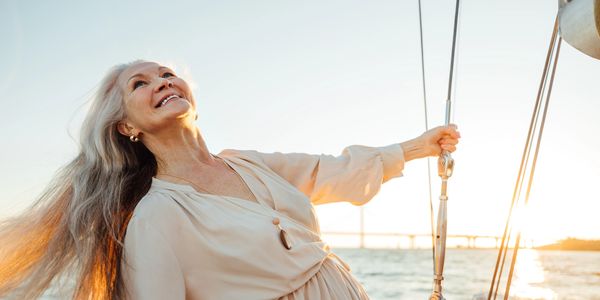 Joyful elderly woman sailing at sunset, smiling and holding a rope.