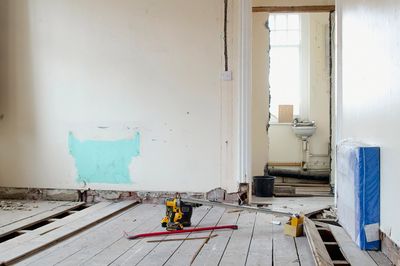 Room under renovation with exposed floorboards and construction tools scattered around.