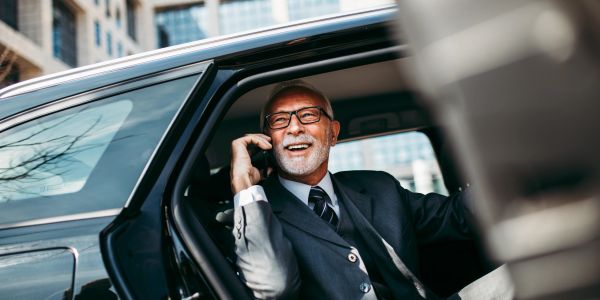 Smiling elderly man talking on phone in car.