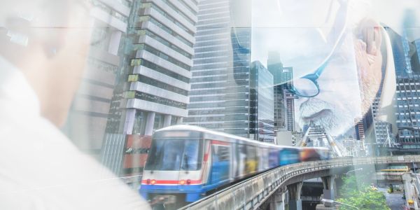 Blurred cityscape with a train and a man wearing glasses.