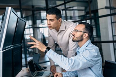 Two men analyzing data on multiple computer screens in an office.