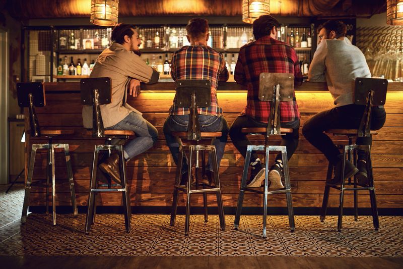 Rear view friends sitting on chairs talking at the bar in a bar. Young people spend their free time chatting in a restaurant.