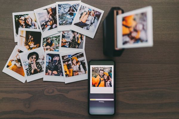 A smartphone prints instant photos beside a pile of printed memories on a wooden table.