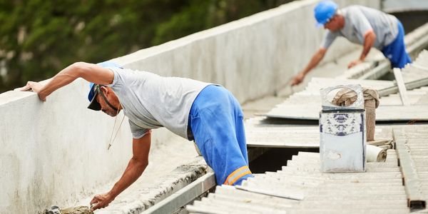 Two construction workers smoothing concrete on a large structure outdoors.