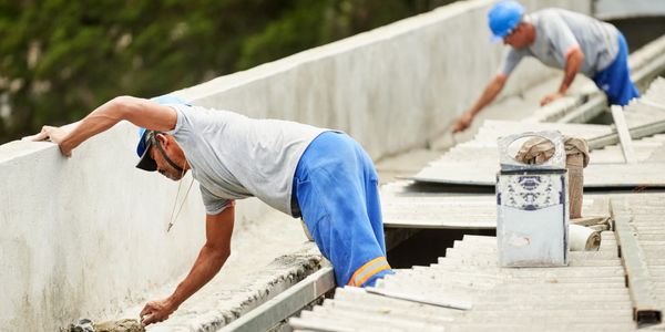 Two construction workers smoothing concrete on a large structure outdoors.