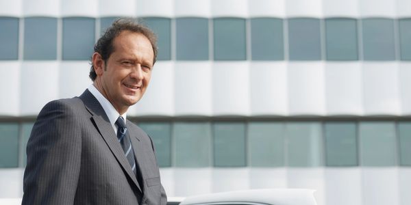 Man in a suit opening a white luxury car door.