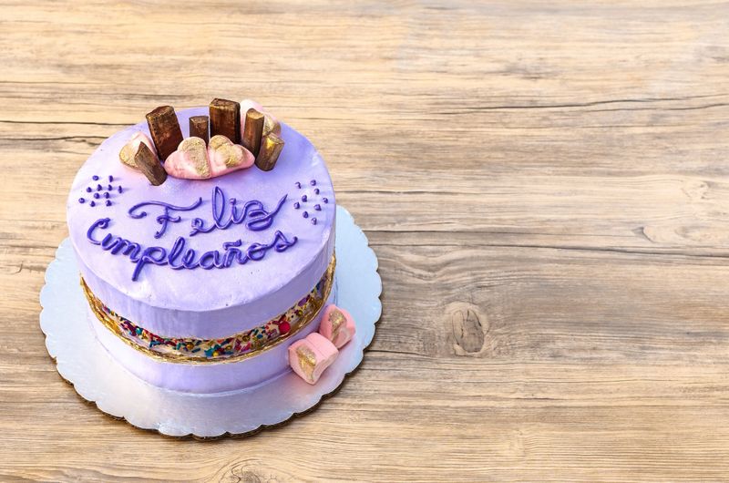 Mauve birthday cake, purple, decorated with chocolates and colorful sparks on a wooden background.