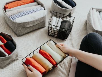 Neatly organized rolled clothes in baskets and bins on a bed.