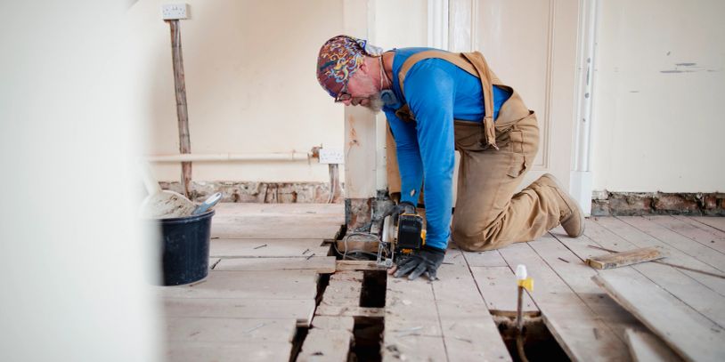 Man cutting wooden floorboards with a power saw.