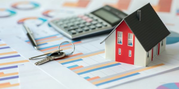 Miniature house with keys and calculator on financial charts.