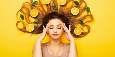 Woman with long hair spread out, decorated with orange slices and green leaves on a bright yellow background.