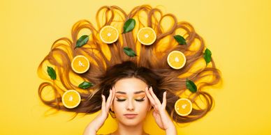 Woman with long hair spread out, decorated with orange slices and green leaves on a bright yellow background.