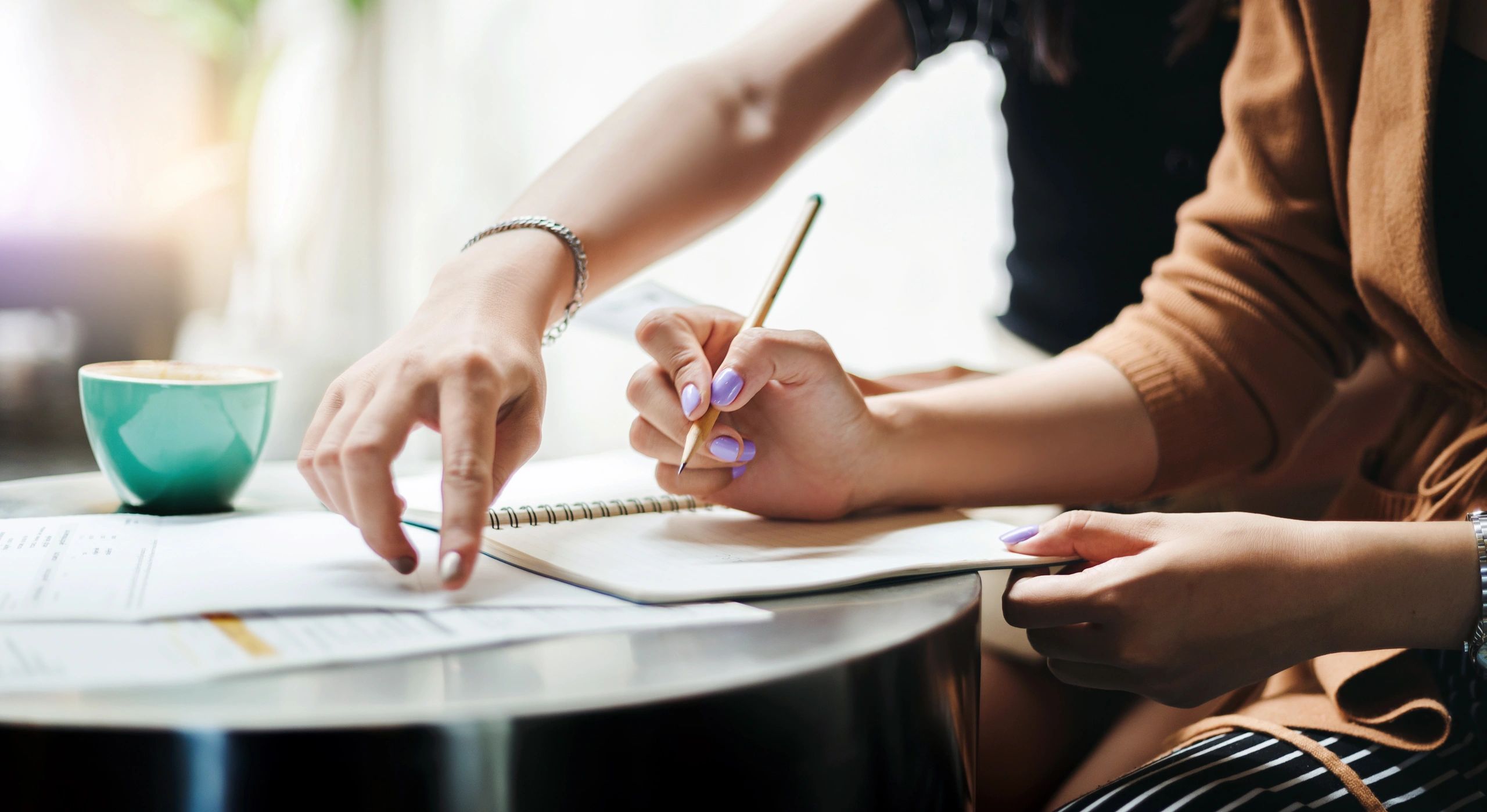 Two people collaborating with notes and a pencil at a table with a cup of coffee.