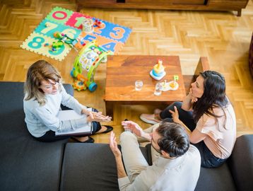 Couple consulting a therapist in a cozy living room with kids' toys.