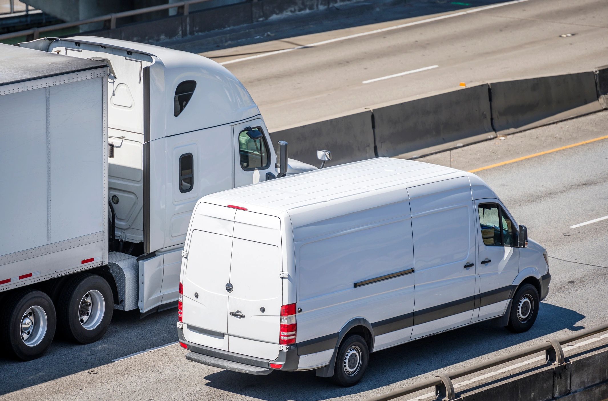 White delivery van and semi-truck on a highway.