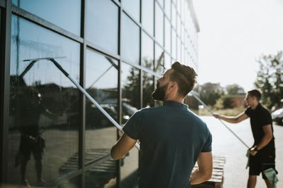 Two men cleaning large glass windows with squeegees outdoors.