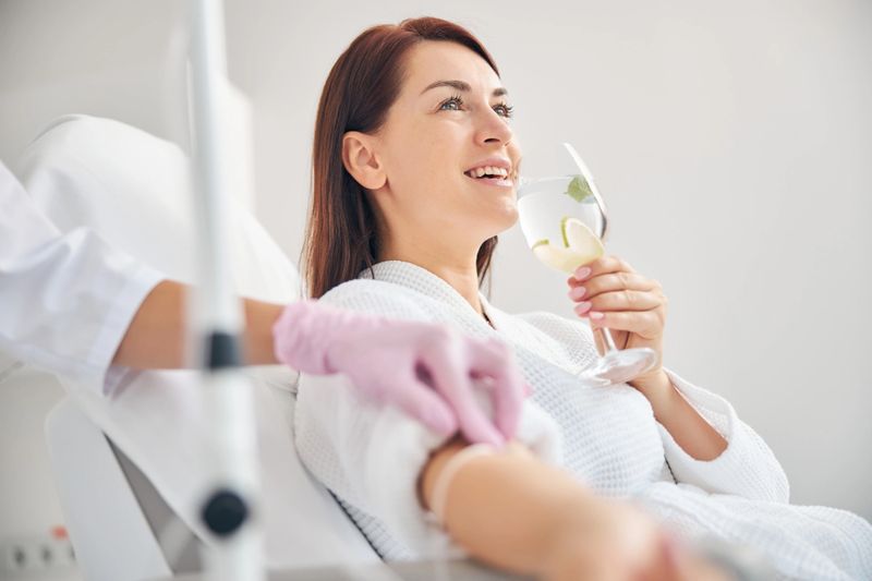 Joyous female patient drinking a healthy beverage during a medical procedure in a beauty clinic