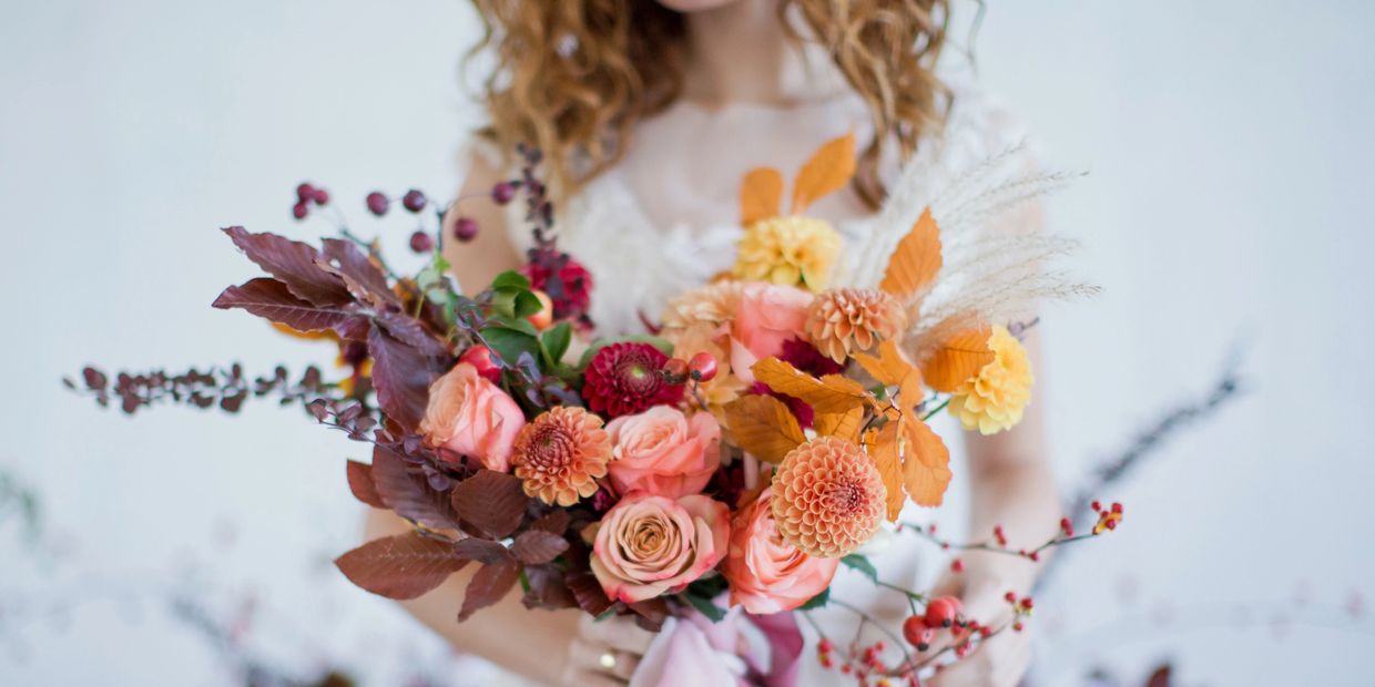 Soft-focus bride holding a large wild bouquet, from dark red to yellow. Fall colors. 