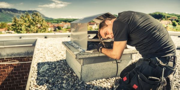 Technician inspecting a rooftop ventilation system on a sunny day.