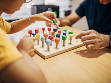 Two people playing a colorful wooden board game together.