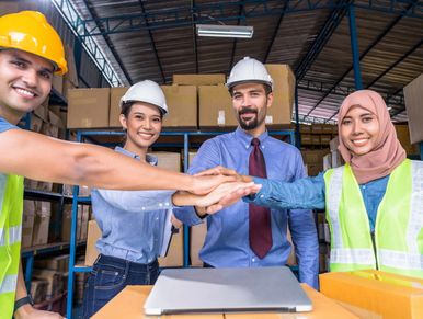 two female workers and two male workers in a warehouse, smiling with outstretched stacked hands