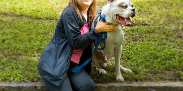 A woman happily posing with her dog outdoors on a grassy area.