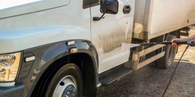 Person washing a white truck with a pressure washer.