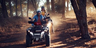 Two people riding ATVs in a forest.