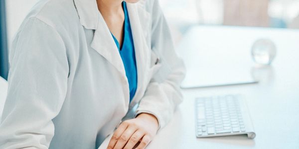 Female doctor in white coat writing on a clipboard at her desk.