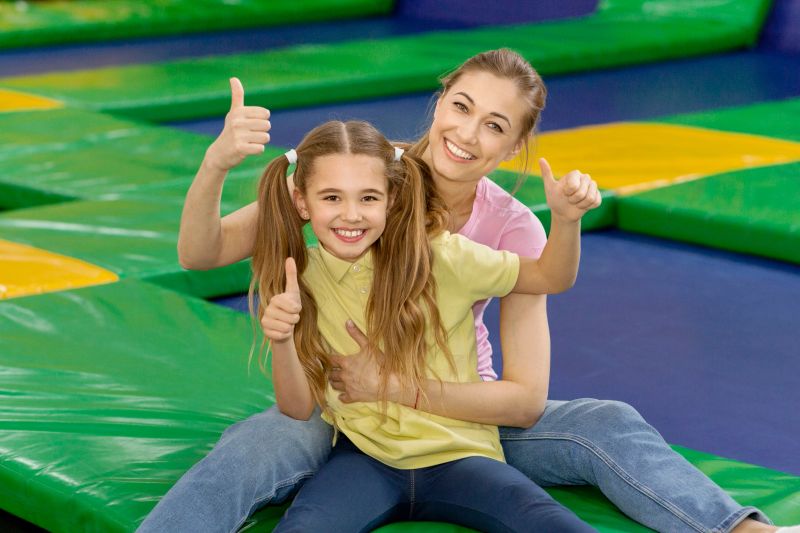 Fun family activities. Mother and her daughter showing thumbs up gesture at indoor trampoline park