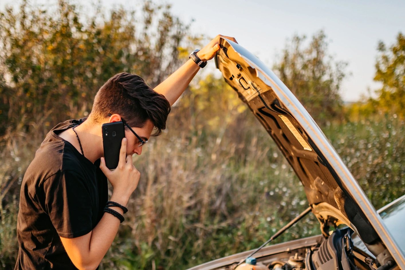Man on phone checking car engine with hood open.