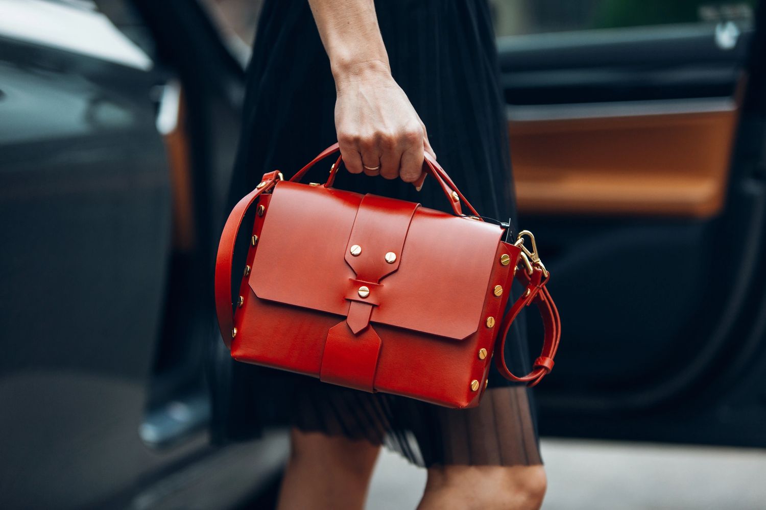 A woman holding a stylish red leather handbag with gold studs.