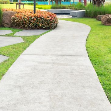 Curved concrete pathway in a green garden with benches and plants.